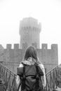 Back view woman with backpack wearing jeans jacket. Fortification, old castle on background. Journey. Vertical photo. Mystical