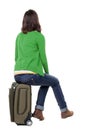 Back view of woman in cardigan who sits on a suitcase. Royalty Free Stock Photo
