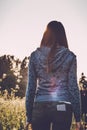 Back view of woman in casual wear enjoying the beauty of sunny autumn day in high grass. Young female in hoodie and jeans standing Royalty Free Stock Photo