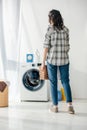 back view of woman in grey shirt and jeans holding basket near washer Royalty Free Stock Photo