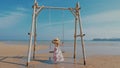 Back view of woman in hat and dress having fun on beach swing. Royalty Free Stock Photo