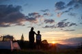 Back view of woman hugging child near camping in mountains at dawn standing on grass with wildflowers Royalty Free Stock Photo