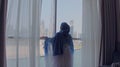 Back view of woman opening curtains and looking out of window to cityscape at hotel in the morning. Modern buildings at Royalty Free Stock Photo