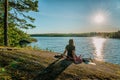 Back view of woman relaxing and enjoys warm evening Sunset on flat stone slope close to river. Scandinavian nature landscape,