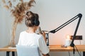Back view on woman sits on table and recording podcast at his small cozy radio studio