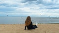 Back view of woman sitting on sandy shore of lake. Concept. Beautiful young woman sitting on sand enjoys view of sea