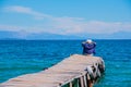 Back view of a woman sitting on a tiny wooden pier by the sea. Young beautiful girl sitting on jetty. Back view. Amazing Royalty Free Stock Photo