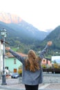 Back view of woman standing with raised hands in mountain village.