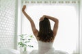 Back of view Woman stretching her arm after wake up on bed and looking outside windows Royalty Free Stock Photo