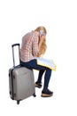 Back view of woman traveler sitting on their suitcases and looking for a route map, talking the phone. Royalty Free Stock Photo