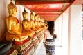 Back view of a woman walking side to aligned golden Buddha Statues at the Emerald temple in Bangkok