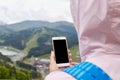 Back view of woman wearing rose jacket and blue backpack, standing at top of mountain, holding her device, no image, looking for Royalty Free Stock Photo