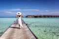 Back view of a woman in white dress walking down a pier over turquoise sea in the Maldives Royalty Free Stock Photo