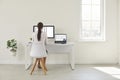 Back view of woman sitting at office desk and working on desktop computer and laptop Royalty Free Stock Photo