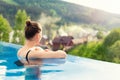 back view young adult female person enjoy relax in infinity edge luxury outdoor swimming pool looking on fog hill green