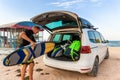 Back view young adult male surfer in wetsuit put out surf board kite equipment on sand beach from van vehicle with Royalty Free Stock Photo