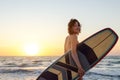 Back view young adult slim sporty female surfer girl with surfboard silhouette stand at ocean coast wave against warm Royalty Free Stock Photo