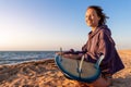 Back view young adult slim sporty female surfer girl with surfboard sitting on sand at ocean coast wave against warm Royalty Free Stock Photo