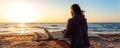 Back view young adult slim sporty female surfer girl with surfboard sitting on sand at ocean coast wave against warm Royalty Free Stock Photo