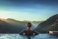 Back view of young adult women enjoy relax in infinity edge luxury outdoor swimming pool. Look green mountains in warm summer