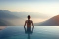 Back view of young adult women enjoy relax in infinity edge luxury outdoor swimming pool. Look green mountains in warm summer