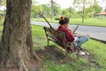 Back view of young asian man in red shirt reading a book on the bench against in beautiful outdoor park. Royalty Free Stock Photo