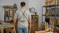 Back view of a young asian man standing thoughtfully in a well-organized carpentry workshop Royalty Free Stock Photo