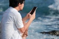 Back view of young Asian man using mobile smart phone at sea shore. Internet of things concept Royalty Free Stock Photo