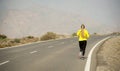 Back view of young attractive sport woman running on desert mountain asphalt road