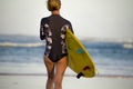 Back view of young attractive and sporty surfer girl in cool swimsuit at the beach carrying surf board into the sea running toward Royalty Free Stock Photo