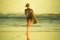 Back view of young attractive and sporty surfer girl in cool swimsuit at the beach carrying surf board into the sea running toward Royalty Free Stock Photo