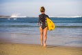 Back view of young attractive and sporty surfer girl in cool swimsuit at the beach carrying surf board into the sea running toward Royalty Free Stock Photo