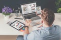 Back view.Young bearded businessman in denim shirt sits in office at table and uses smartphone with charts,diagrams Royalty Free Stock Photo