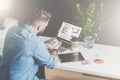 Back view.Young bearded businessman in shirt sits in office at table and uses smartphone with charts,diagrams