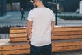 Back view. Young bearded hipster man dressed in white t-shirt and sunglasses is stands on city street. Mock up. Royalty Free Stock Photo