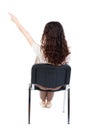 Back view of young beautiful woman sitting on chair and pointin