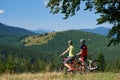 Back view of young bikers couple, man and woman standing with bikes on grassy hill