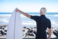 Back view of young blond teenager in the wet suit looking at the sea from the rocky beach holding the surfboard - healthy sport Royalty Free Stock Photo