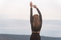 Back view on young blond woman in black clothes with raised her hands up. Sense of freedom