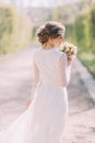 Back view of young blonde bride in white dress looking at bridal bouquet outdoor Royalty Free Stock Photo