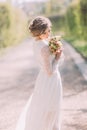 Back view of young blonde bride in white dress looking at bridal bouquet outdoor Royalty Free Stock Photo