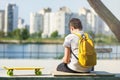 Back view of a young boy with yellow backpack and skateboard in the city park. Trendy student sitting outdoor Royalty Free Stock Photo