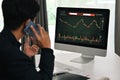 Back view of young businessman having phone conversation and monitoring stocks data candle charts on screen