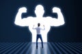 Back view of young businessman with very strong illuminated shadow flexing muscles on dark wall background. Personal development, Royalty Free Stock Photo