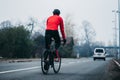 Back view of a young cool male cyclist in red sportswear riding a bicycle on a gloomy day