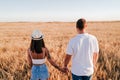 Back view of young couple holding hands in a yellow field at sunset. Love and Summer time Royalty Free Stock Photo