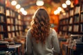 back view of a young curly woman in a light sweater stands in a bookstore among the shelves with books