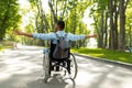 Back view of young disabled black man in wheelchair spreading his arms, feeling happy and free on walk at city park Royalty Free Stock Photo