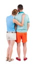 Back view of young embracing couple in shorts hug and look.