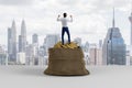 Back view of young european businessman celebrating success on huge sack filled with golden coins on light city background. Wealth Royalty Free Stock Photo